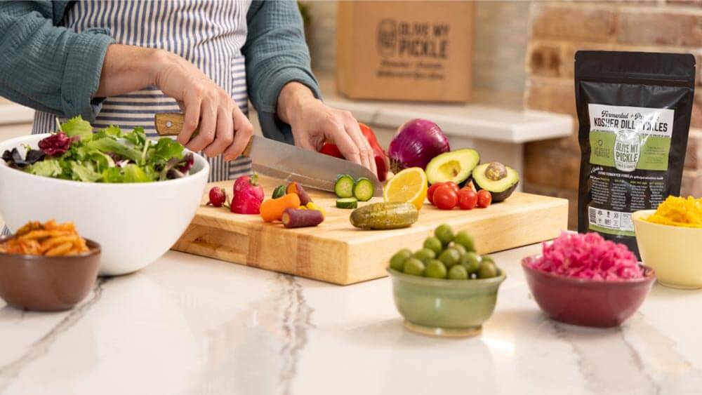 Hands chopping fresh fruits and vegetables on a cutting board with olives in the foreground 